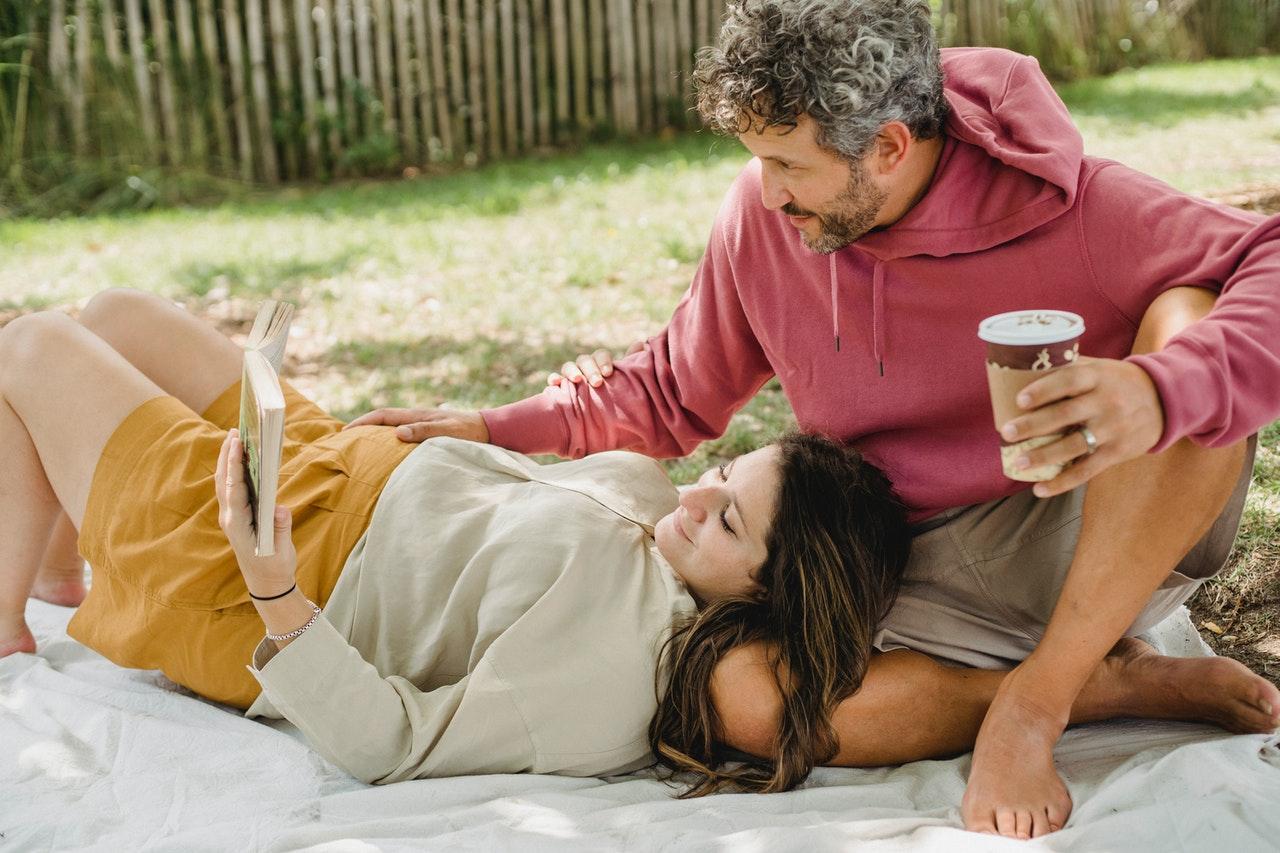 Pregnant woman relaxing with partner for picnic coffee